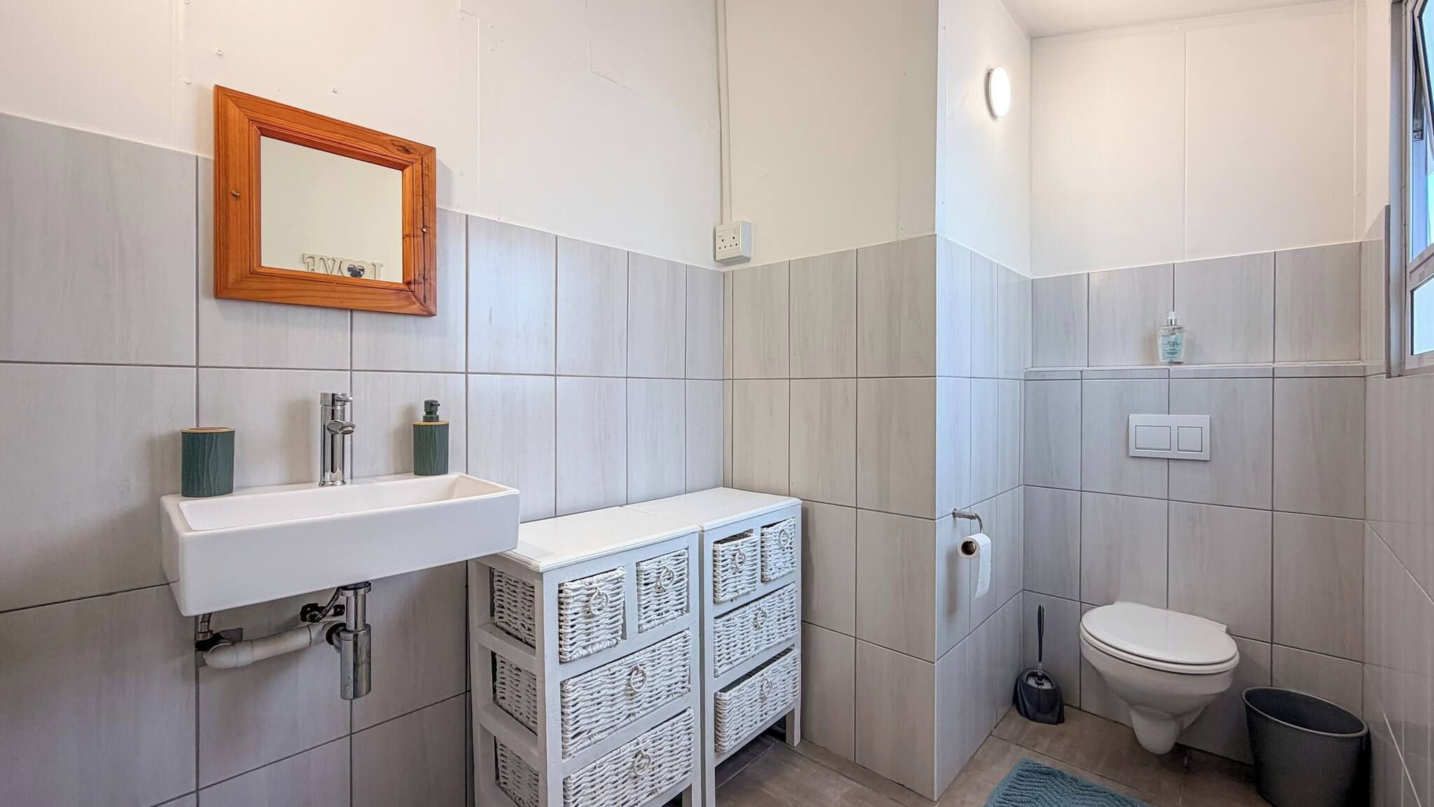 A bathroom with a white sink, a mirror, a toilet, and a small window.