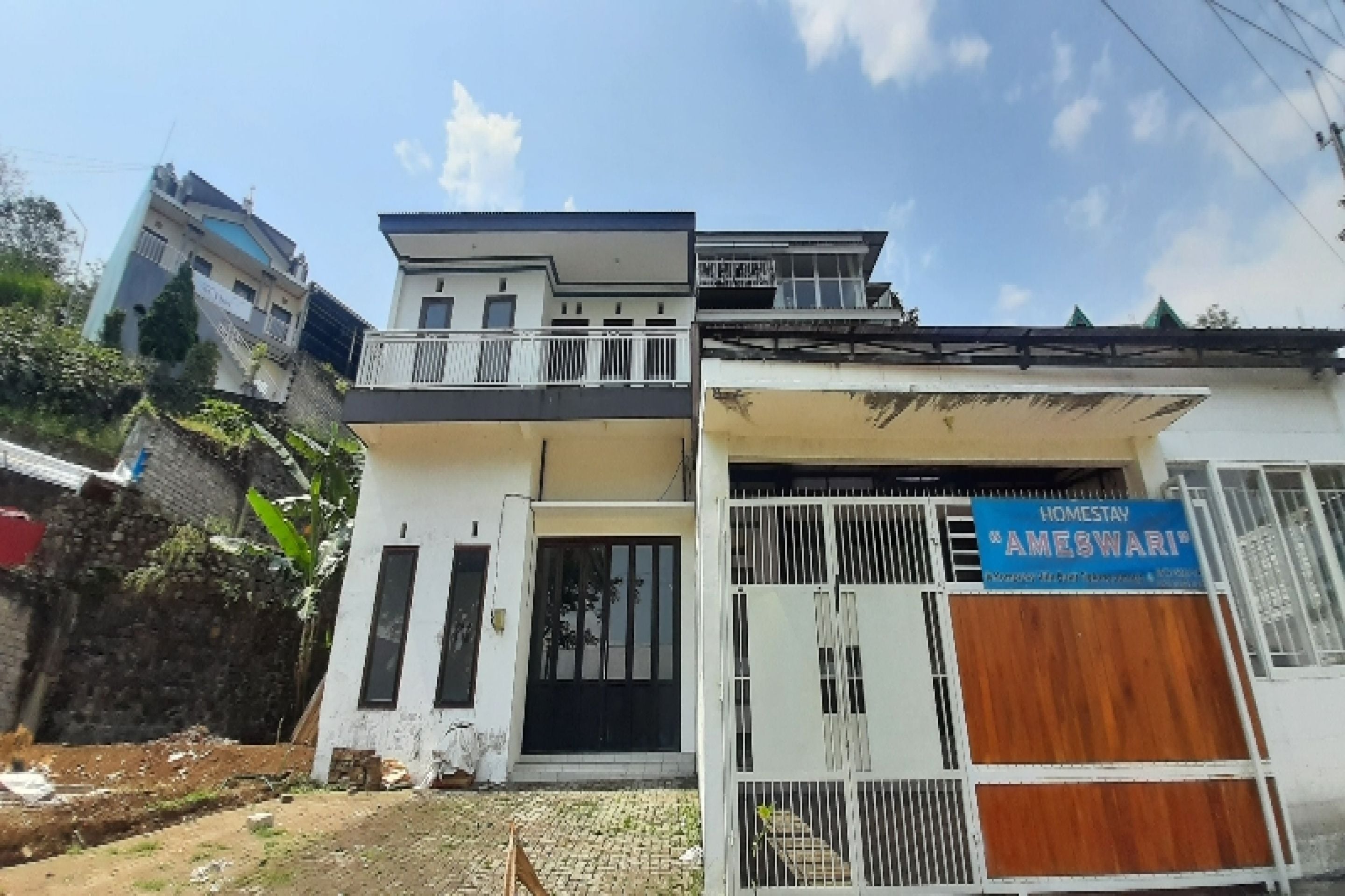 A two-story building with a balcony on the upper floor, a gated entrance, and a sign indicating a homestay.