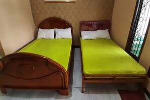 Dos llits individuals amb estructura de fusta i matalassos verds en una habitació amb paper pintat i una finestra amb reixatge metàl·lic.