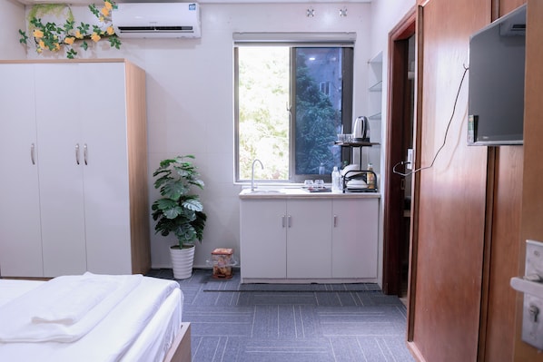 A compact hotel room with a bed, a small kitchenette, a potted plant, and a window with a view of greenery. - Homestay Adam Hà Đông (Kien Hung)