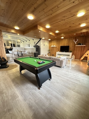 A pool table in a room with wooden walls and ceiling, a sofa, and a television. - Charming house for 8 people, with a pool table and an enclosed garden (Sacquenville)