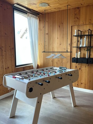 A foosball table in a room with wooden walls and a window with curtains. - Charming house for 8 people, with a pool table and an enclosed garden (Sacquenville)