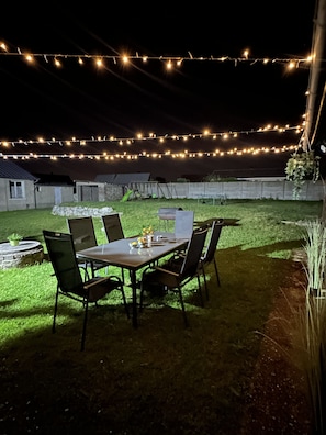 An outdoor dining area with a table and chairs, surrounded by a stone wall and a grassy lawn. - Charming house for 8 people, with a pool table and an enclosed garden (Sacquenville)