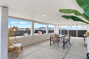 Eine überdachte Terrasse mit Tisch und Stühlen, großen Fenstern und Blick auf die Berge.