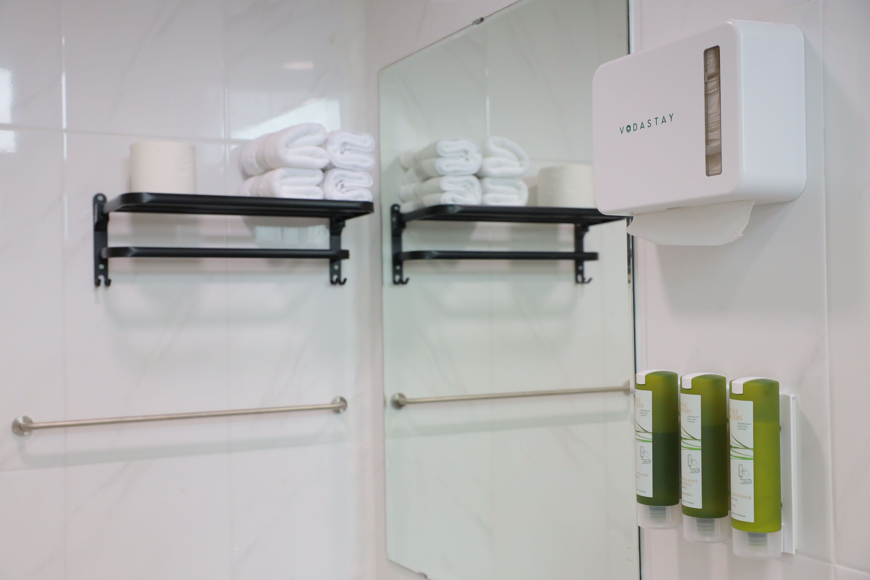 Een badkamer met handdoekrekken, een handdroger en groene flessen shampoo en conditioner.