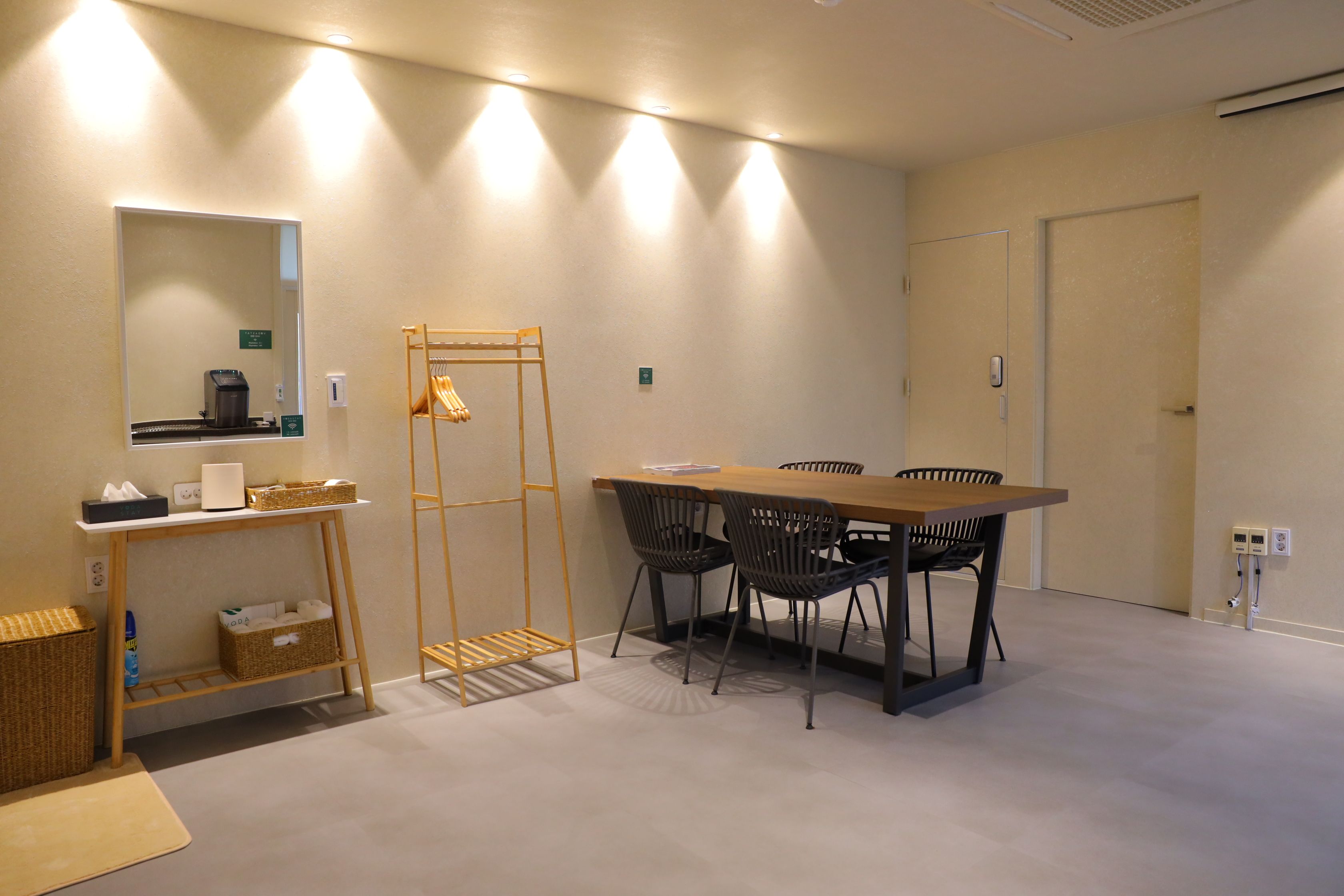 Een vergaderruimte met een houten tafel, zwarte stoelen, een kledingrek en een spiegel aan de muur.