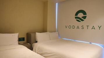 Een hotelkamer met twee bedden, een minibar en een logo van VODASTAY op de muur.