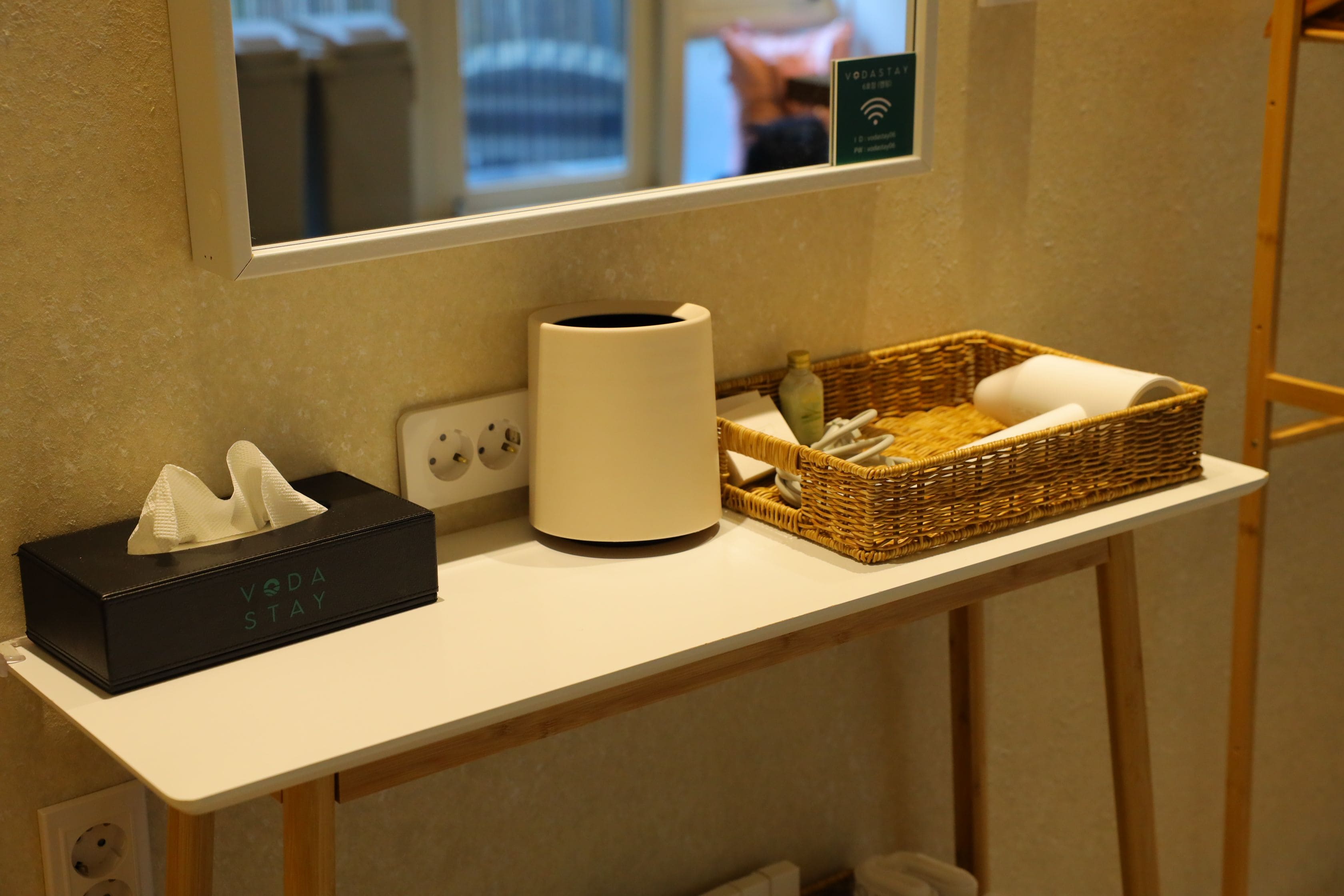 A bathroom counter with a tissue box, a white cylindrical container, and a wicker basket with toiletries.