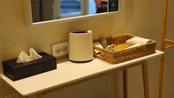 Una encimera de baño con un dispenser de pañuelos, un recipiente cilíndrico blanco y una cesta de mimbre con artículos de aseo.