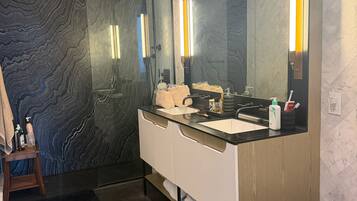 A modern bathroom with a large mirror, dark marble walls, and a white vanity.