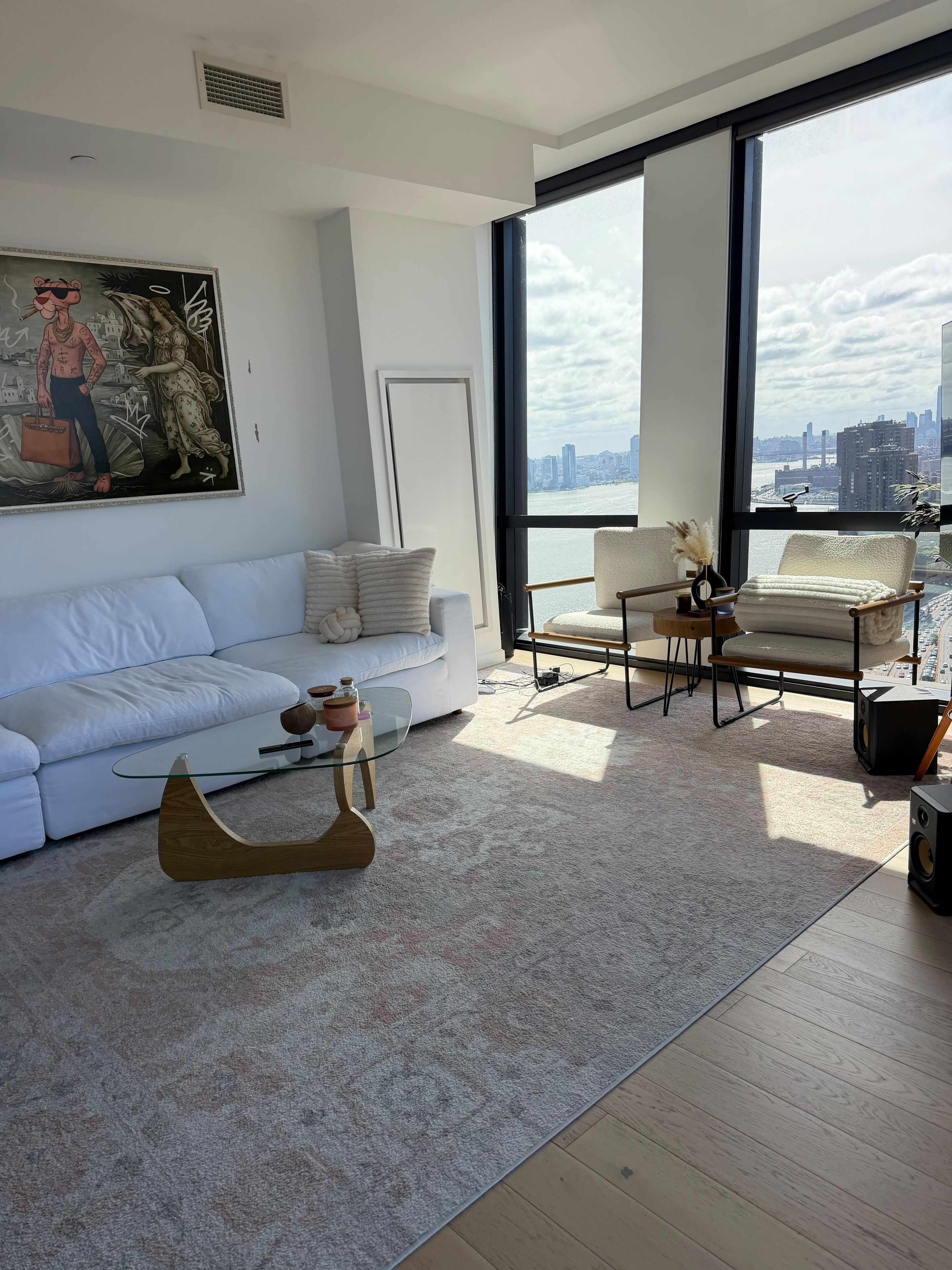 A modern living room with a white sofa, a glass coffee table, and a view of a city skyline through large windows.