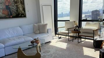 A modern living room with a white sofa, a glass coffee table, and a view of a city skyline through large windows.