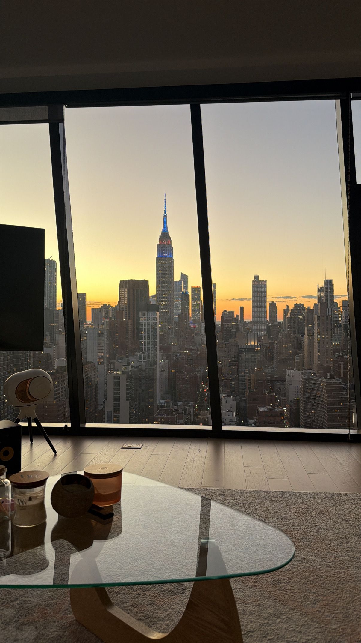 A room with a large window overlooking a city skyline at sunset.