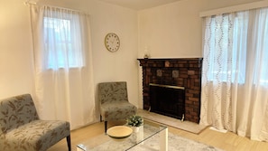 A living room with a fireplace, two armchairs, a coffee table, and a clock on the wall. - Bright & Cozy Retreat Near Shops & Subway (North York)