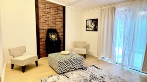 A living room with a brick wall, two armchairs, a patterned ottoman, a rug, and a framed picture on the wall. - Bright & Cozy Retreat Near Shops & Subway (North York)