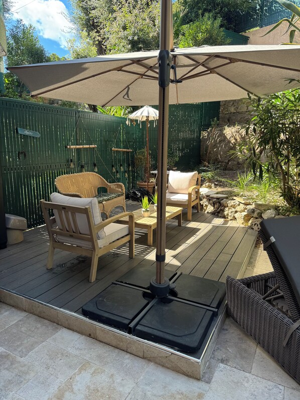 Un patio exterior con cubierta de madera, mobiliario de mimbre y una sombrilla grande.