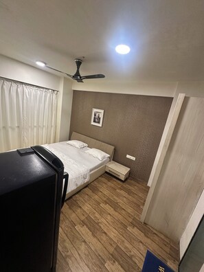Un dormitori amb un llit, un ventilador de sostre, una taula de nit i una làmpada de paret.