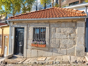 A stone building with a tiled roof, a black door, and a window with a metal grille. - A Window to Porto - Corticeira Lovely House (Porto)