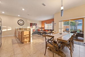 A spacious kitchen with a dining area, a living room with a sofa and a coffee table, and a large window providing a view of the outdoors. - Family 4BR, Private Pool, Resort Amenities (Four Corners)