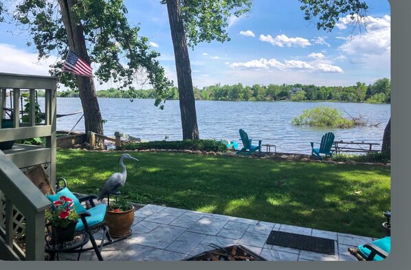 A lakeside patio with a deck, chairs, and a bird.
