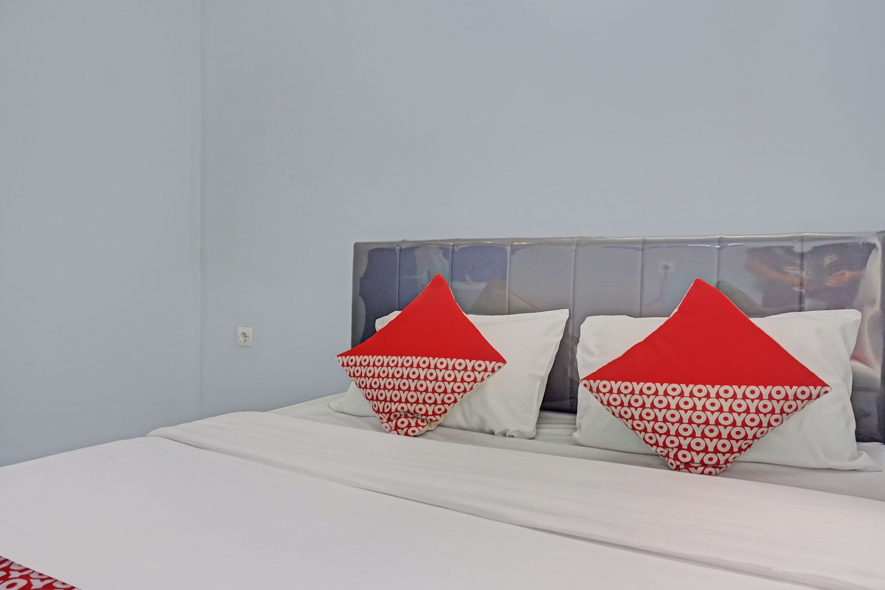 A bed with a white mattress and two pillows with a red and white pattern.