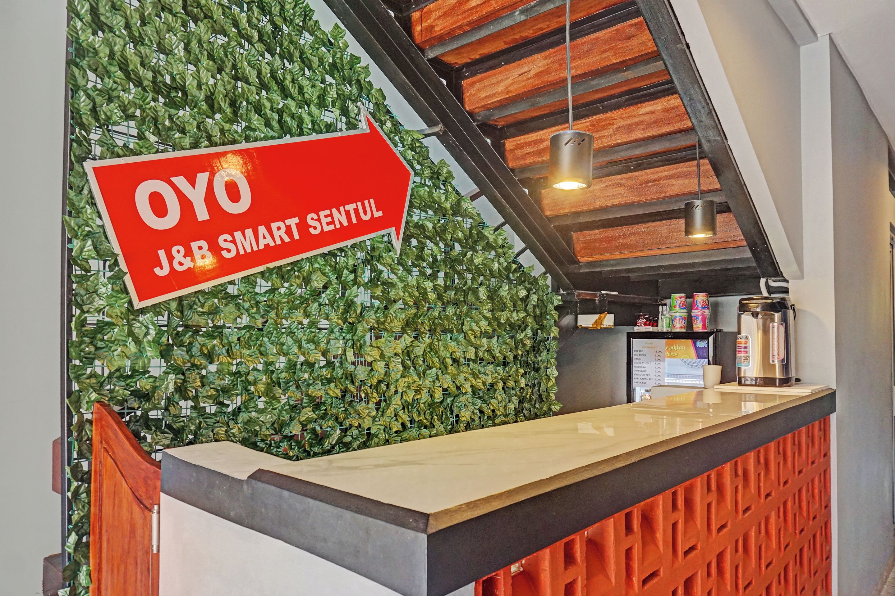 Una reception con una parete verde e lussureggiante e un cartello rosso che indica 'OYO J&B SMART SENTUL'.
