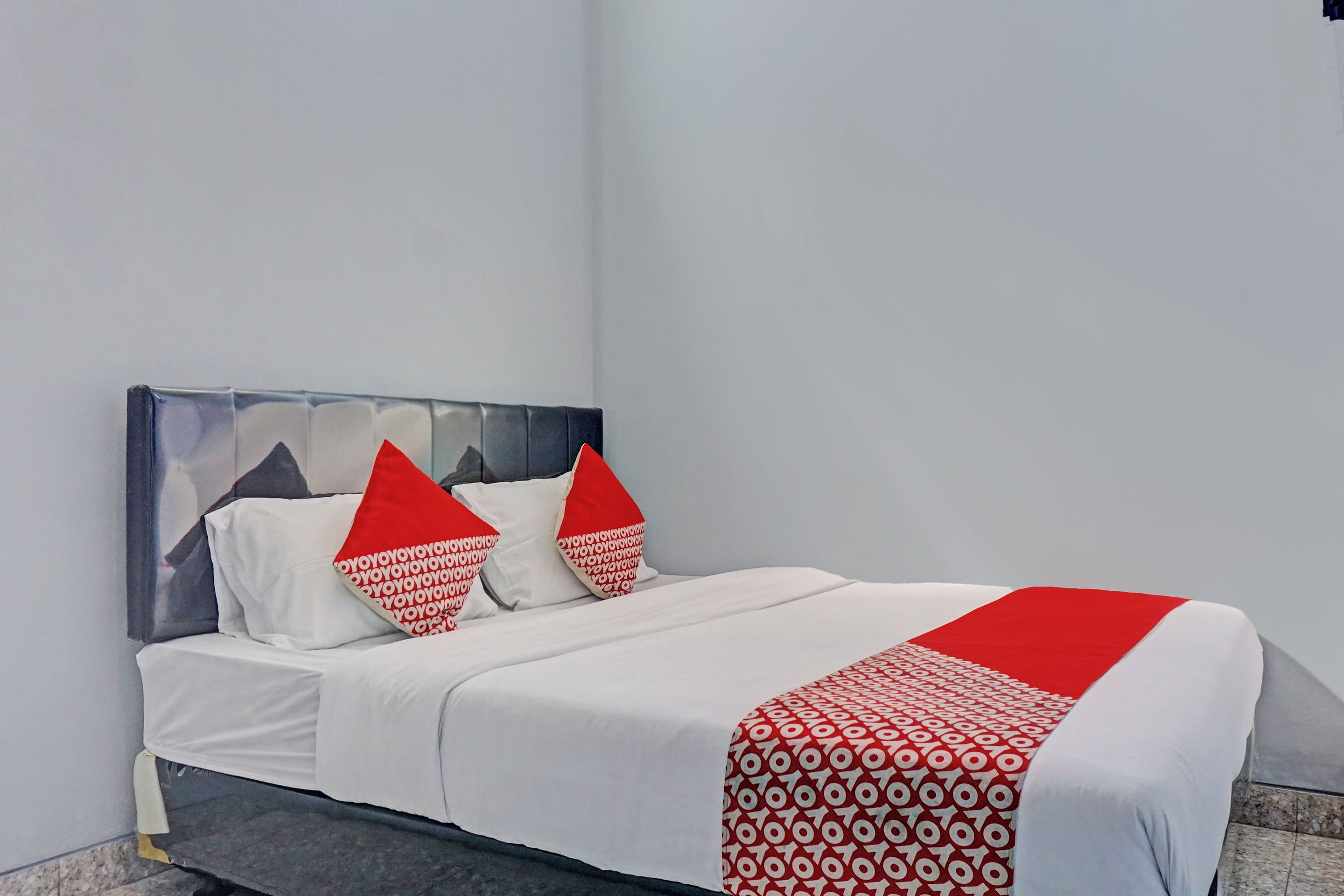 Un lit avec une literie blanche et des oreillers rouges, une tête de lit grise et un couvre-lit à motifs rouges et blancs.