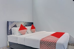 A bed with white bedding and red pillows, a grey headboard, and a red and white patterned throw.