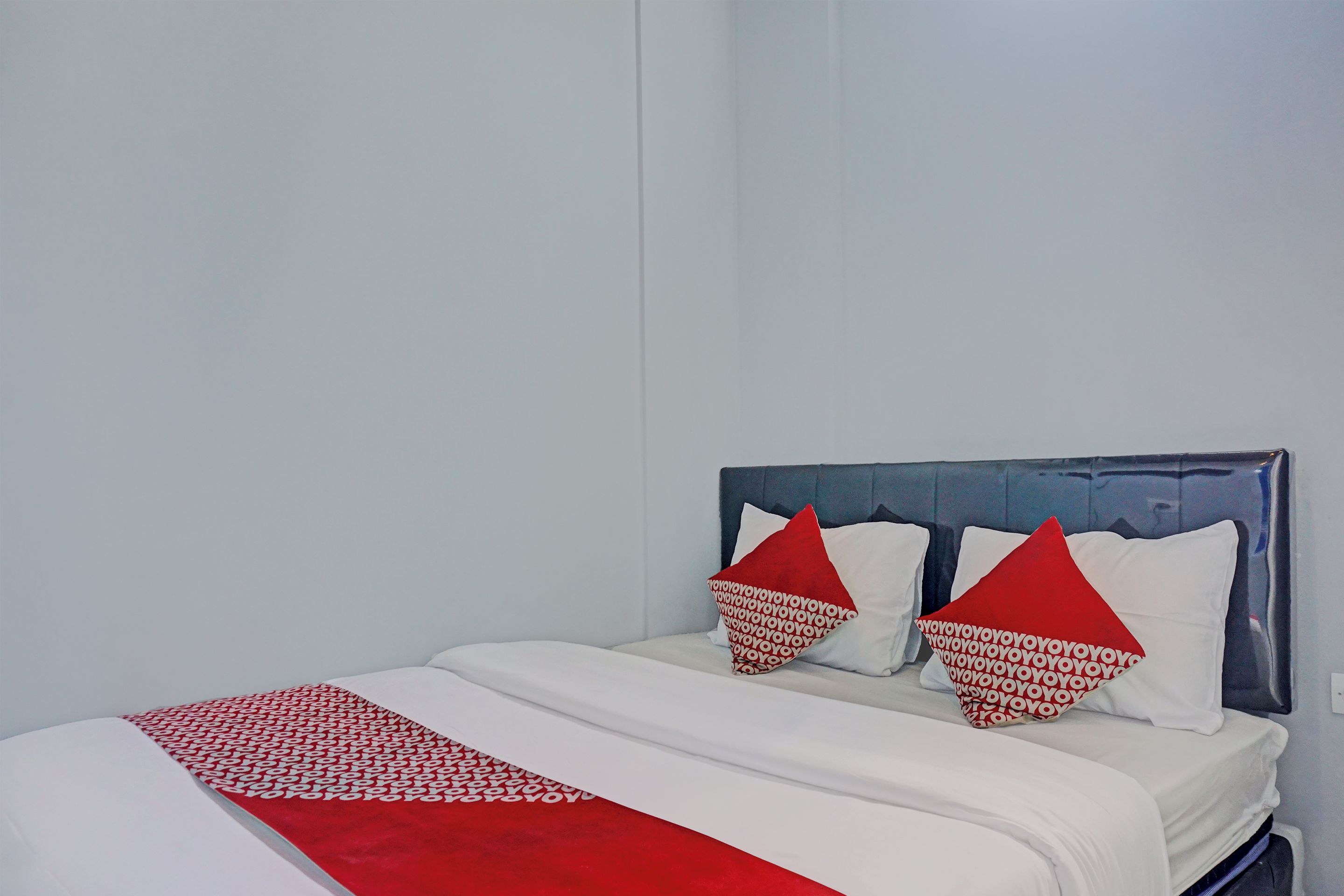 Una cama con cubrecolcha blanco y rojo, dos almohadas con estampado rojo y blanco, y un cabecero oscuro.