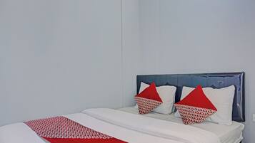 Una cama con cubrecolcha blanco y rojo, dos almohadas con estampado rojo y blanco, y un cabecero oscuro.