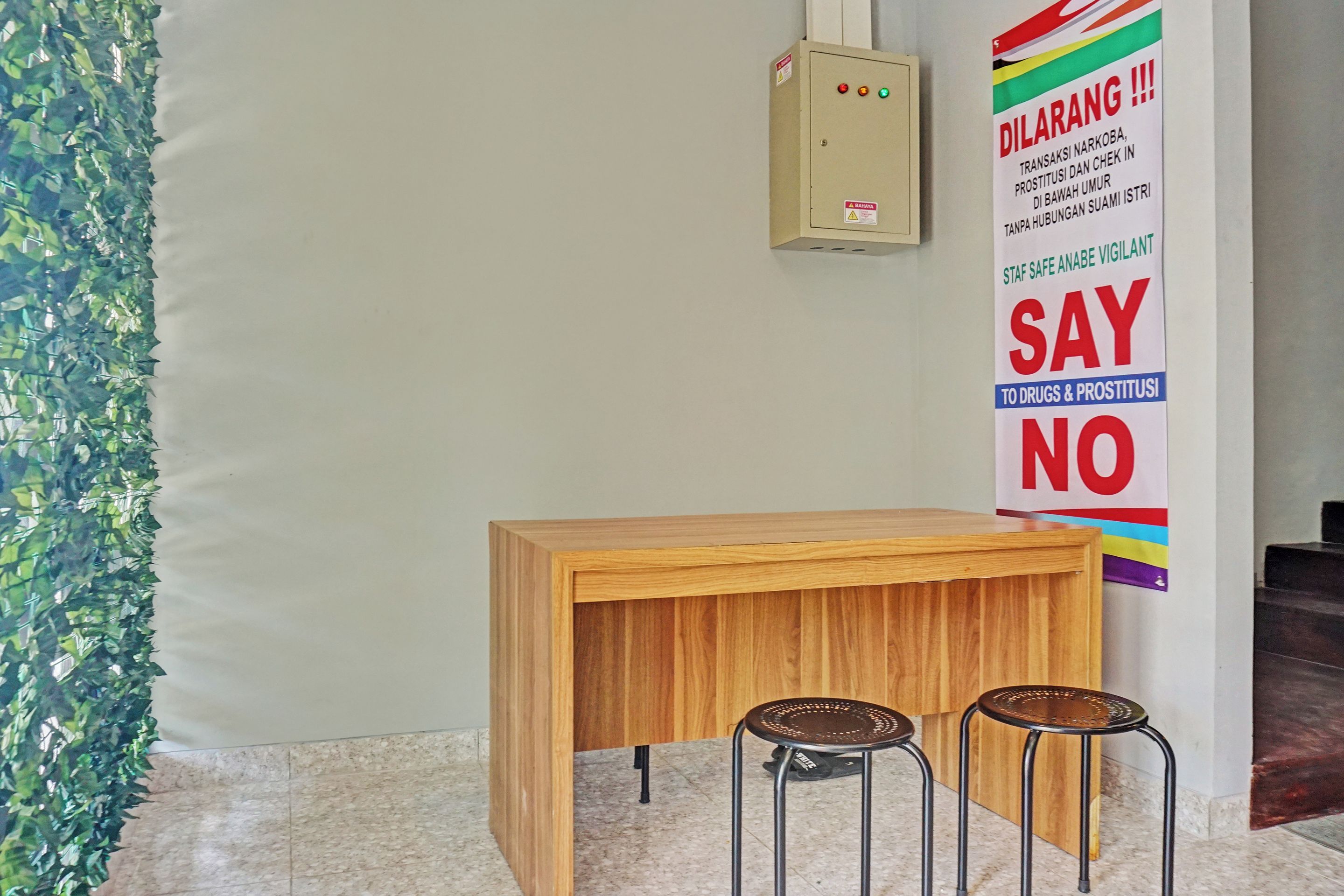 A wooden desk with two stools, a wall-mounted electrical box, and a poster with a 'SAY NO' message.