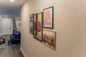 A hallway with framed artwork on the wall, a sofa, and a rug. - The Hudson Residence- Luxury 2BR-Parking-Near NYC (Union City)