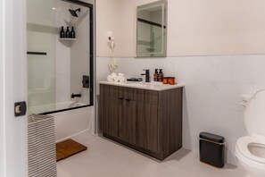 Moderni kylpyhuone, jossa on suihku, wc ja pesuallas sekä hygieniatarvikkeita.