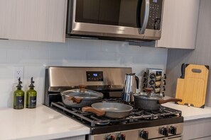 A kitchen with stainless steel appliances, including a microwave, oven, and stove. There are two pots on the stove, a kettle, and a wooden cutting board. - The Hudson Residence- Luxury 2BR-Parking-Near NYC (Union City)