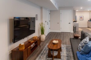 Ein modernes Wohnzimmer mit Fernseher, Holzmöbeln, einer Zimmerpflanze und einer Couch mit Kissen.