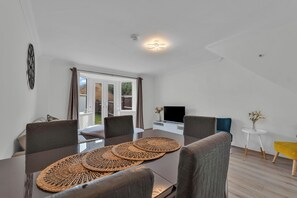 A modern living room with a dining area, a TV, and a view of the outdoors. - Spacious 3-Bed Home | 4 Mins to Universal Studios | Parking & Fast WiFi (Marston Moretaine)