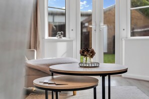 Ein Zimmer mit einem runden Tisch und einem kleineren runden Tisch, beide mit schwarzen Beinen, und einer Vase mit Blumen auf dem größeren Tisch.