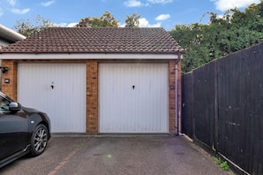 Eine Garage mit zwei weißen Türen, einer Ziegelwand und einem schwarzen Zaun.
