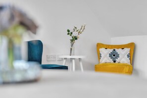 A modern room with a blue chair, a yellow sofa with a patterned pillow, and a white table with a vase of flowers. - Spacious 3-Bed Home | 4 Mins to Universal Studios | Parking & Fast WiFi (Marston Moretaine)
