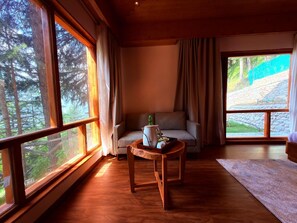 Une pièce confortable avec un canapé, une petite table et une vue sur une forêt, visible à travers de grandes fenêtres.