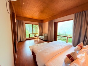Une chambre dotée d’un grand lit, d’un canapé et offrant une vue sur un paysage verdoyant par les fenêtres.