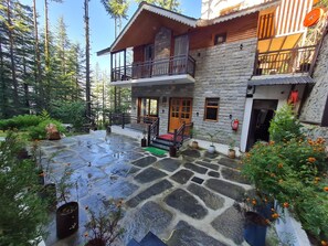 A stone building with a balcony, surrounded by trees and potted plants.