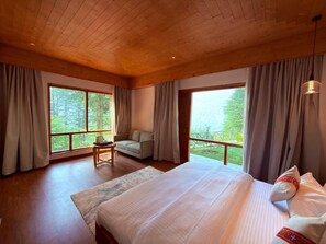 Une chambre avec un grand lit, une chaise et une vue sur une forêt par les fenêtres.