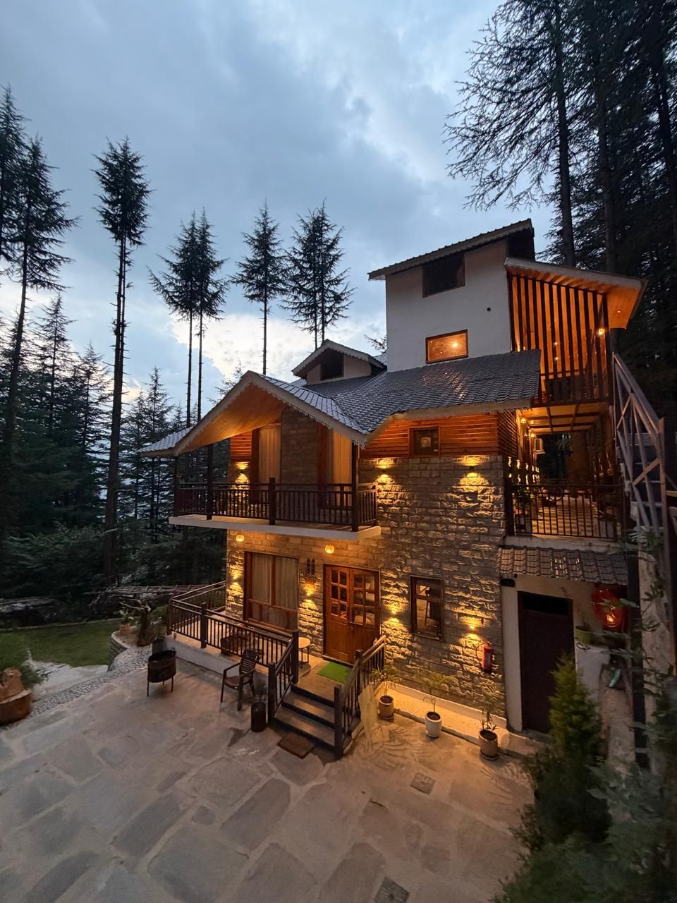 A multi-level stone house with a balcony, surrounded by trees.