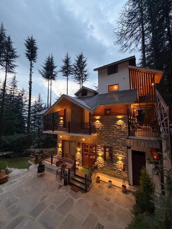 A multi-level stone house with a balcony, surrounded by trees.