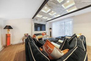Una sala moderna con un sofá negro, un televisor de pantalla plana y vistas urbanas a través de grandes ventanales.