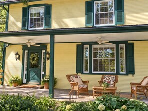 A two-story house with a porch, green shutters, and wicker furniture. - Hopewell Creek Farm - Amish Country Farmhouse, Creek & Fall Color - Sleeps 8 (Lancaster)
