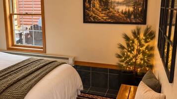 Un dormitorio con cama, ventana, un cuadro, un pequeño árbol con luces y un banco.