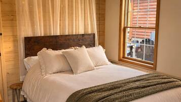 A bedroom with a large bed, a wooden headboard, a window with a view, and a hanging light fixture.