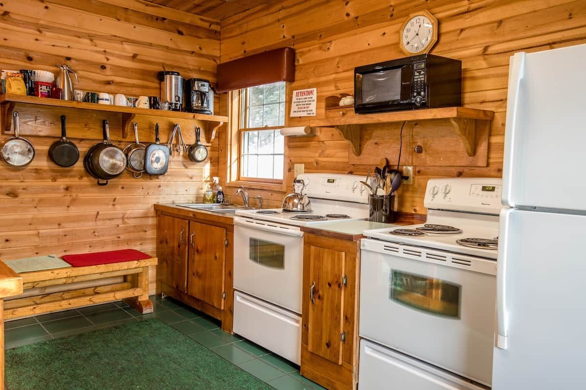 A wooden cabin kitchen with a stove, microwave, and hanging pots.